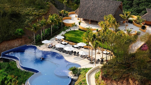 Ein Resort mit großem Schwimmbad, Liegebereichen und strohgedeckten Gebäuden.