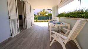 A balcony with a table set for two, white chairs, and a view of a garden and palm tree. - House Villino Azzurro at 50 meters from the beach (Marina di Grosseto)