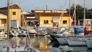 A marina with several boats docked, a building with a sign reading "Nautica Pesca Bar", and a lifebuoy visible on a boat. - House Villino Azzurro at 50 meters from the beach (Marina di Grosseto)
