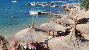 A beach with thatched umbrellas, a pier with boats, and clear blue water. - Apartment with pool, air conditioning, WLAN, barbecue (Pula)
