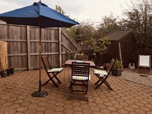 Un patio con una mesa y sillas de madera, una sombrilla azul y una cerca de madera al fondo.