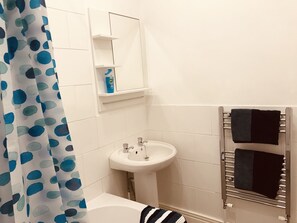 Un baño con lavamanos blanco, un espejo, un perchero con dos toallas y una cortina de ducha con lunares azules y verdes.