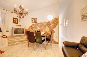 A modern living room with a stone wall, a chandelier, a dining table with chairs, a television, and a leather sofa. - Apartment with outdoor pool, air conditioning, WLAN and barbecue (Pula)