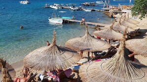 A beach with thatched umbrellas, a pier with boats, and clear blue water.