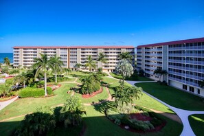 A hotel with multiple floors, a central courtyard with palm trees, and a view of the ocean. - A Little Slice of Paradise !! (Bonita Springs)