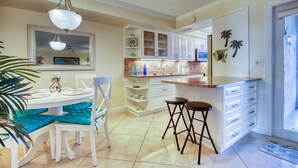 A kitchen with white cabinets, a dining table with teal cushions, and a bar area with stools. - A Little Slice of Paradise !! (Bonita Springs)