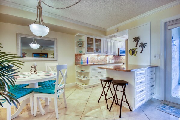 Una cocina con armarios blancos, una mesa de comedor con cojines color turquesa y una zona de bar con taburetes.