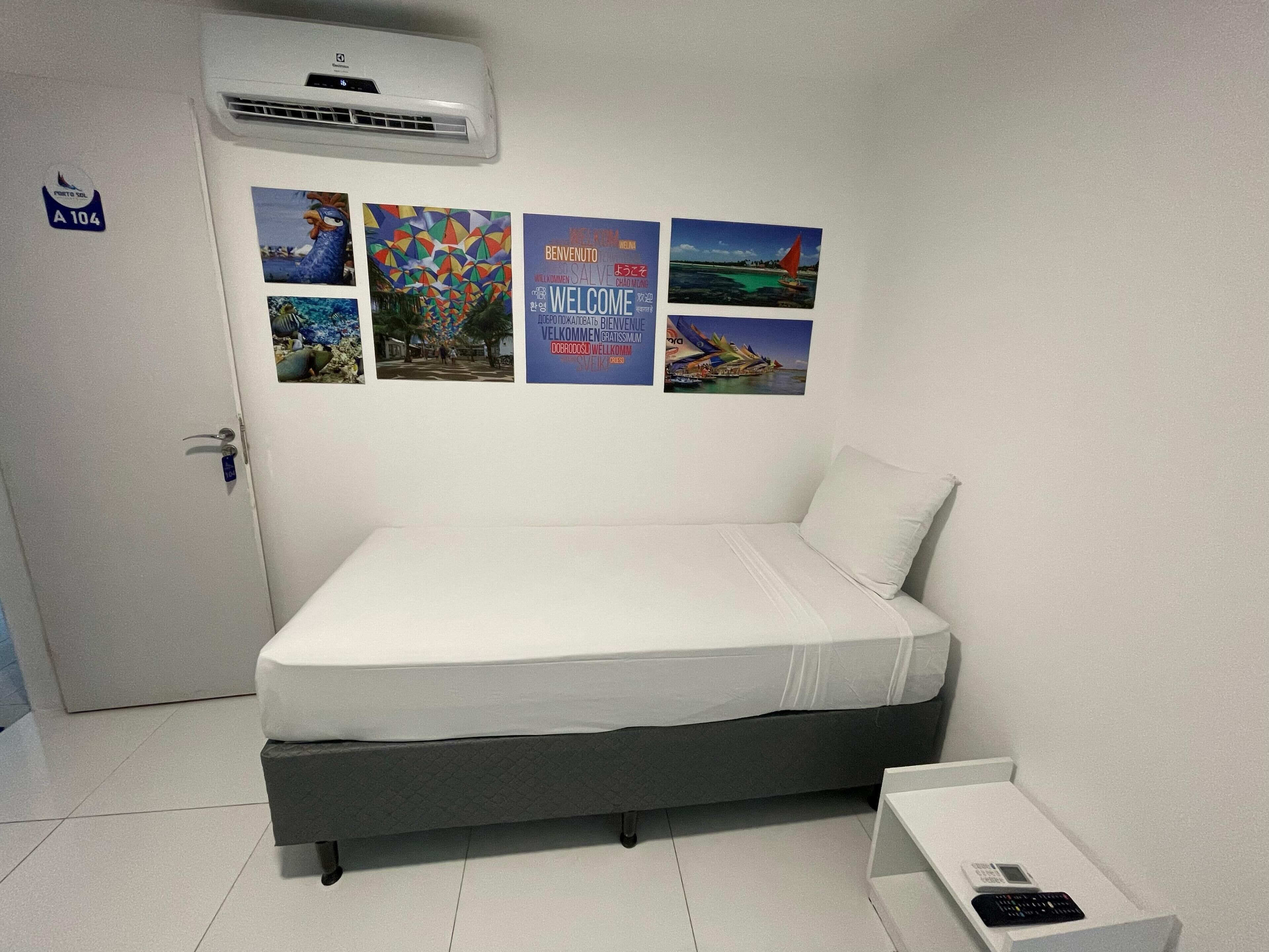 A room with a bed, a small table, and a wall-mounted air conditioner. There are four pictures on the wall.