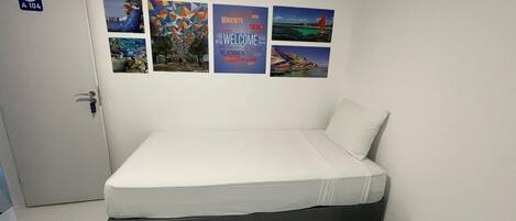 A room with a bed, a small table, and a wall-mounted air conditioner. There are four pictures on the wall.