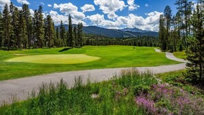 A golf course with a clear path, surrounded by tall pine trees and mountains in the background. - Spacious Remodel, 4br, Minutes To Conf Center & Slopes! 4 Bedroom Condo by RedAwning (Keystone)