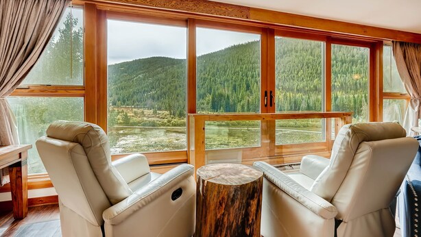 A room with two leather chairs, a wooden table, and large windows offering a view of a forested mountain. - Spacious Remodel, 4br, Minutes To Conf Center & Slopes! 4 Bedroom Condo by RedAwning (Keystone)