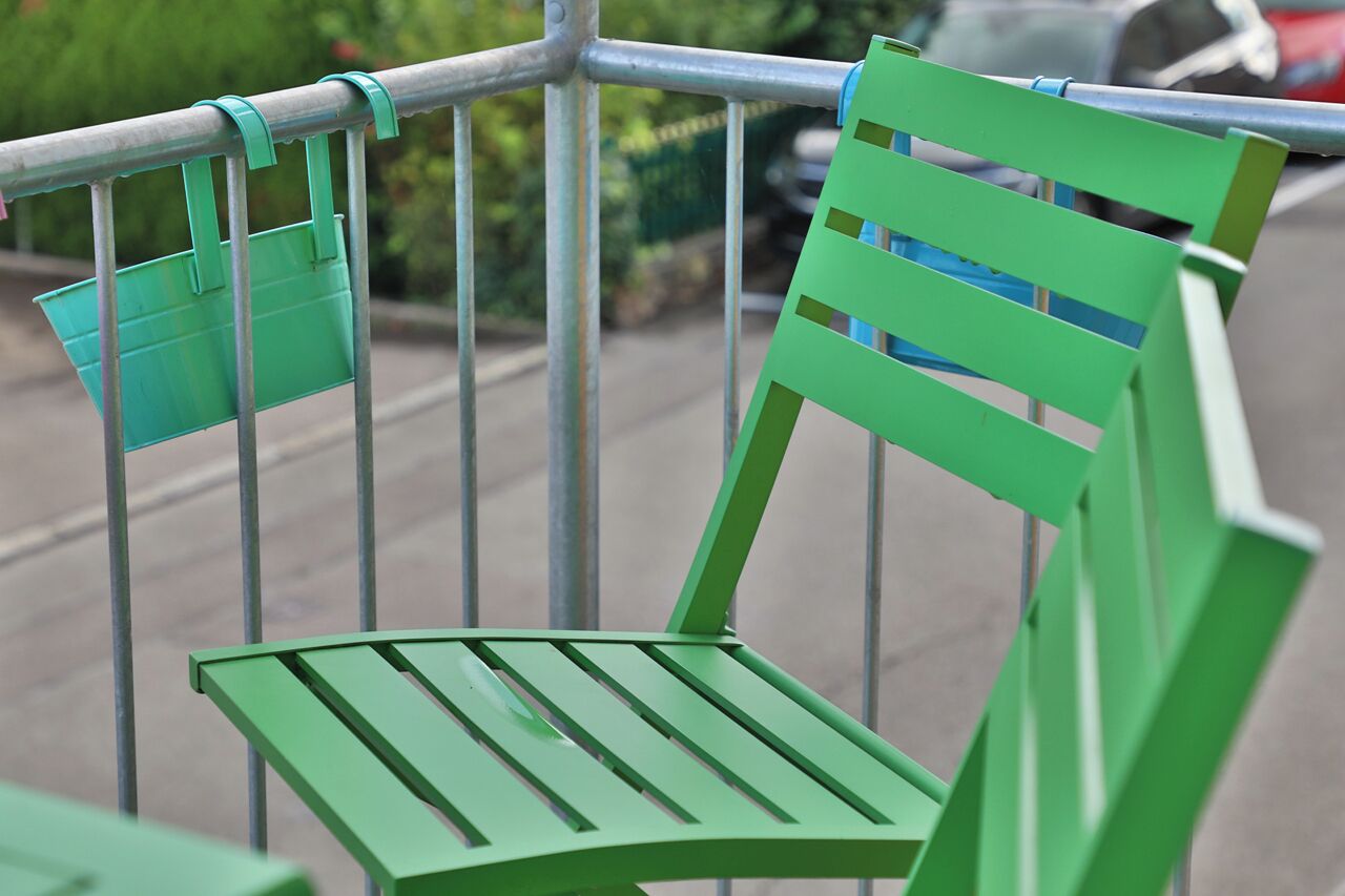 A green chair with a metal frame, attached to a metal railing.