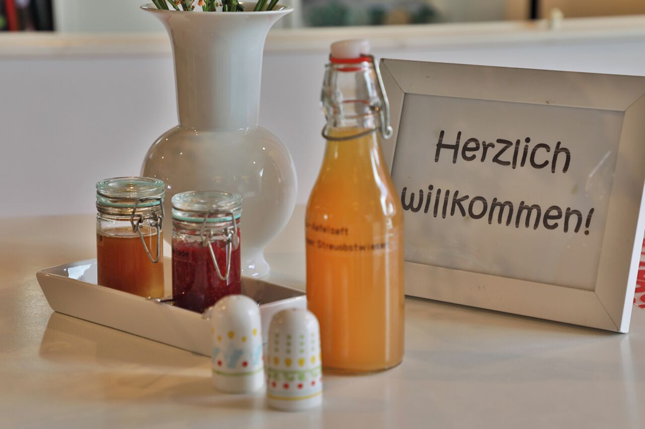 Ein Tisch mit einem Schild, das „Herzlich willkommen!“ zeigt, sowie verschiedenen Gläsern und Flaschen.