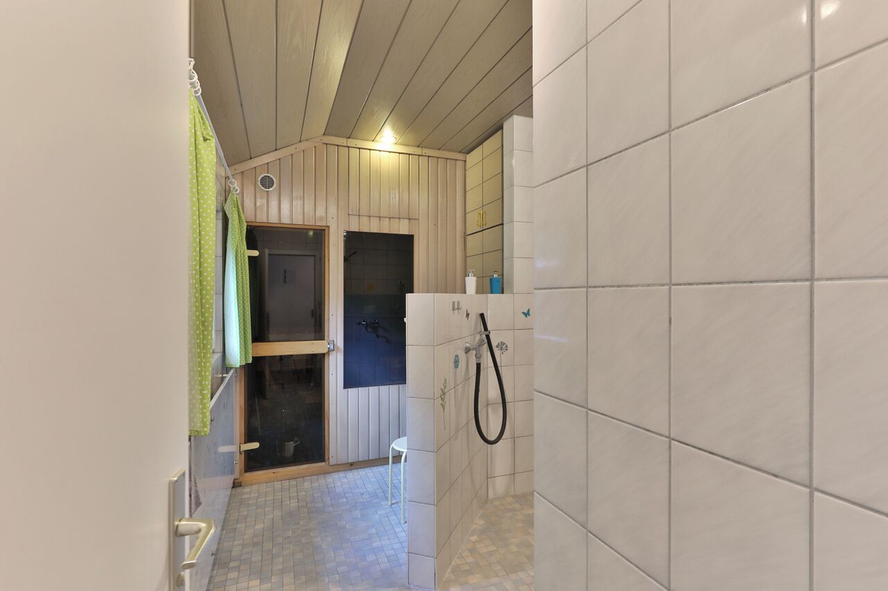 Ein schmales Badezimmer mit Dusche, gefliesten Wänden und Holzboden.