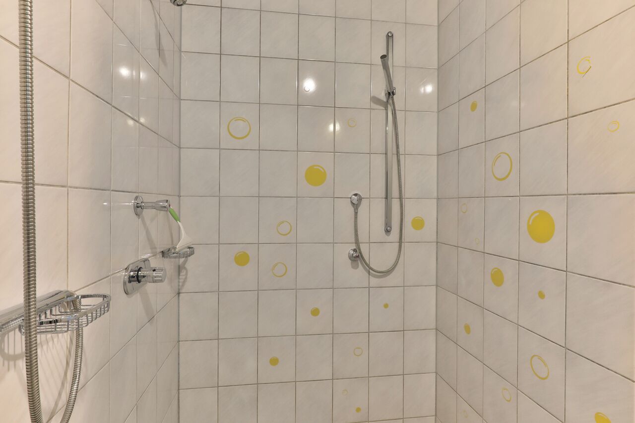 A shower area with white tiles and yellow circles, a handheld showerhead, and a wall-mounted faucet.