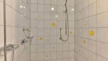 A shower area with white tiles and yellow circles, a handheld showerhead, and a wall-mounted faucet.