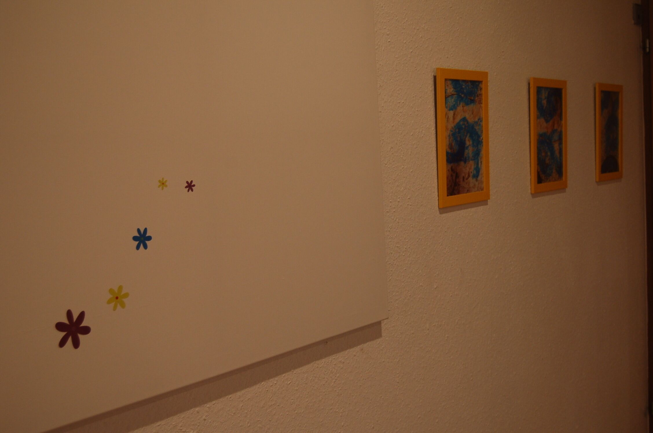 A wall with three framed artworks and five flower decals.