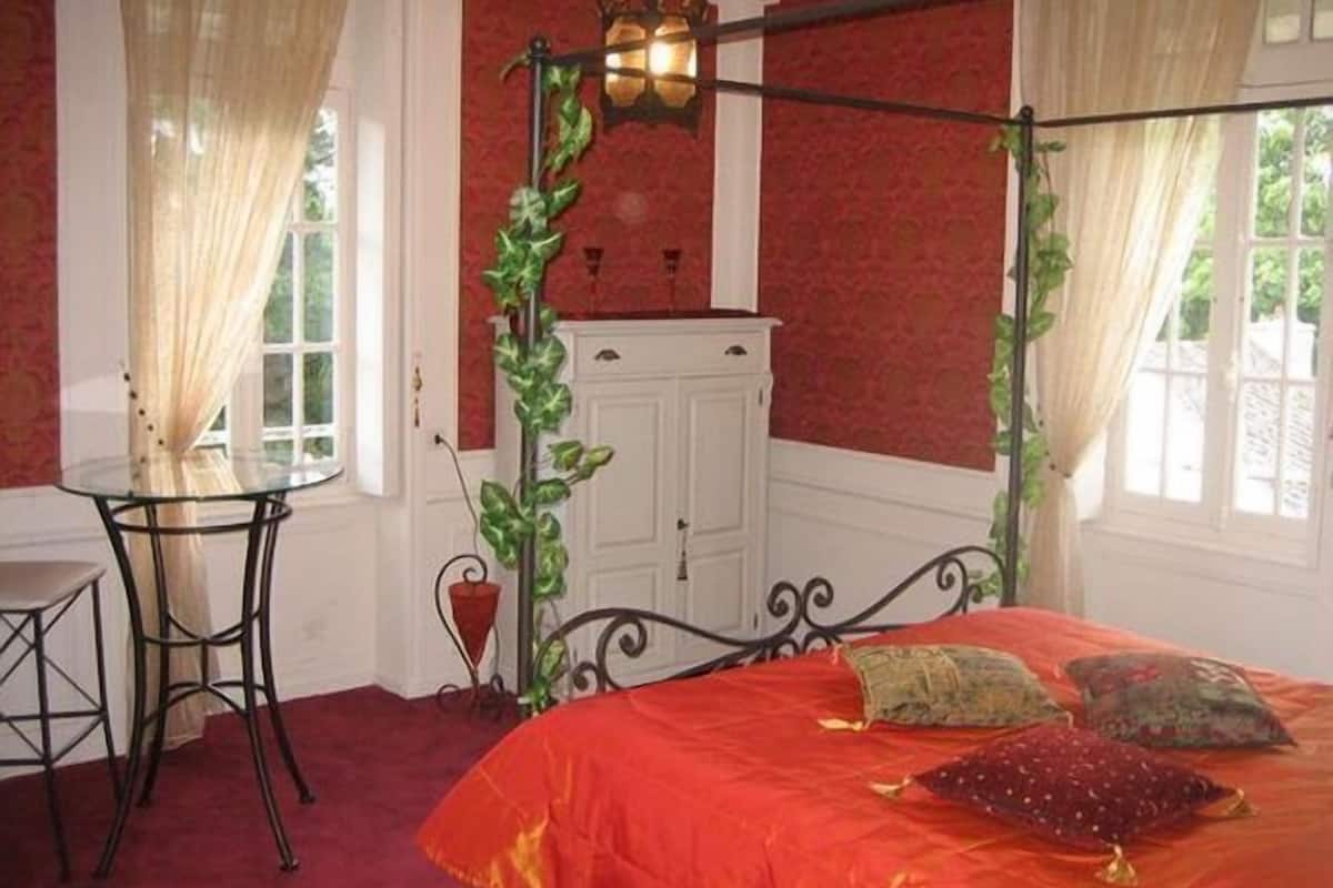 Une chambre avec un lit à baldaquin, une petite table avec une chaise et un buffet.