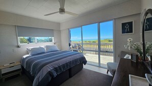 Ein Schlafzimmer mit einem großen Bett, einem Schreibtisch und Blick auf den Strand durch eine Schiebetür.