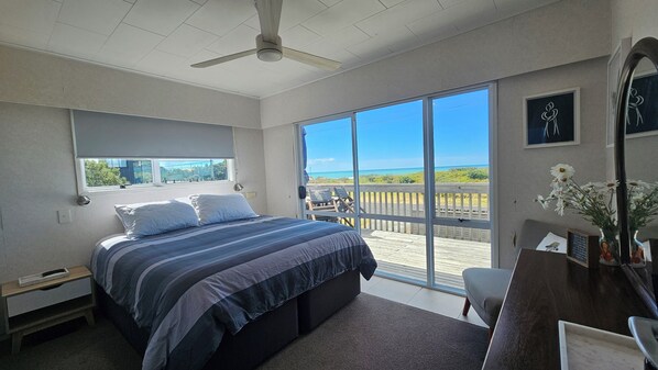A bedroom with a large bed, a desk, and a view of the beach through a sliding glass door.