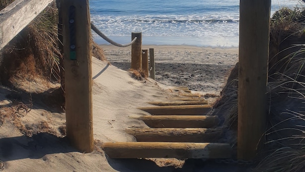 Eine Holztreppe führt zu einem Strand mit freiem Blick auf den Ozean.