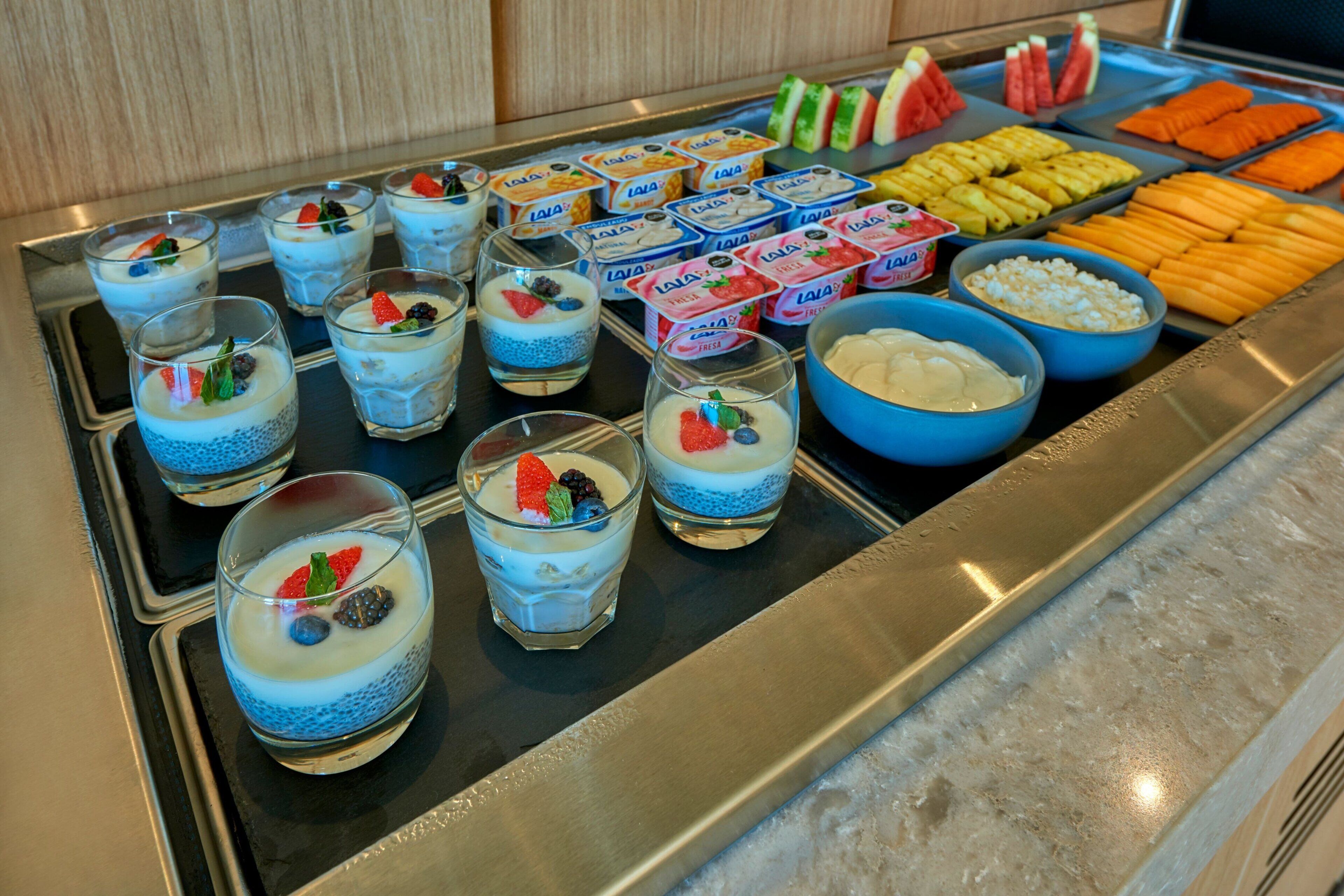 Un bufé con diversas opciones de comida, incluyendo parfait de yogur, frutas frescas y salsas.