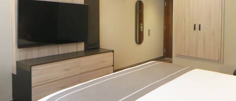 A bedroom with a bed, a TV mounted on the wall, a dresser, a mirror, and a wardrobe.