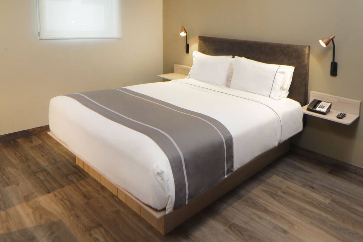 Un letto rifatto con cura, con copripiumino a righe, una testiera in legno, comodini con lampade e un telefono sul tavolino di fianco al letto.