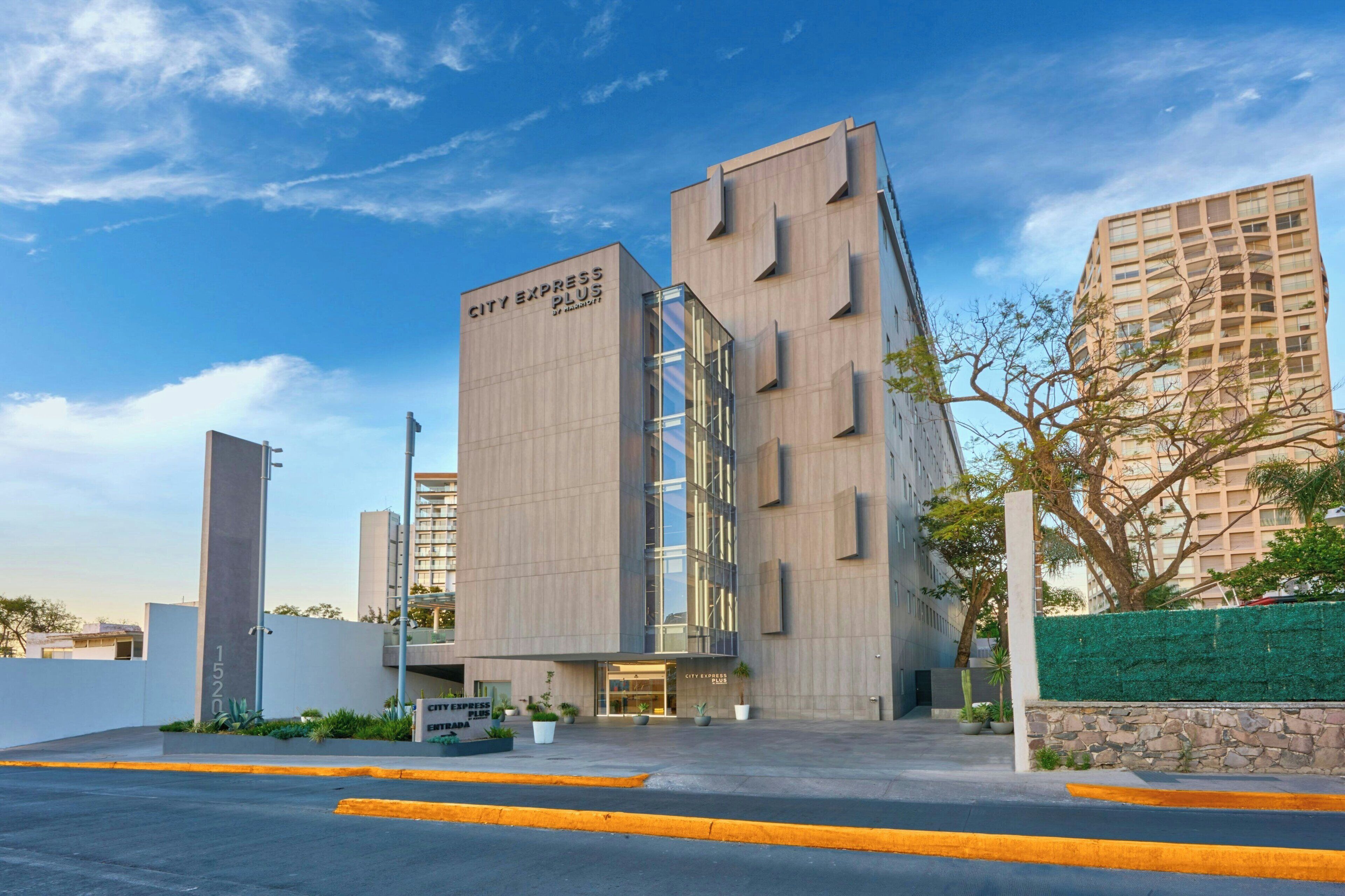 A modern hotel with a prominent 'City Express Plus' sign, featuring a clean, rectangular facade with large windows and a flat roof.