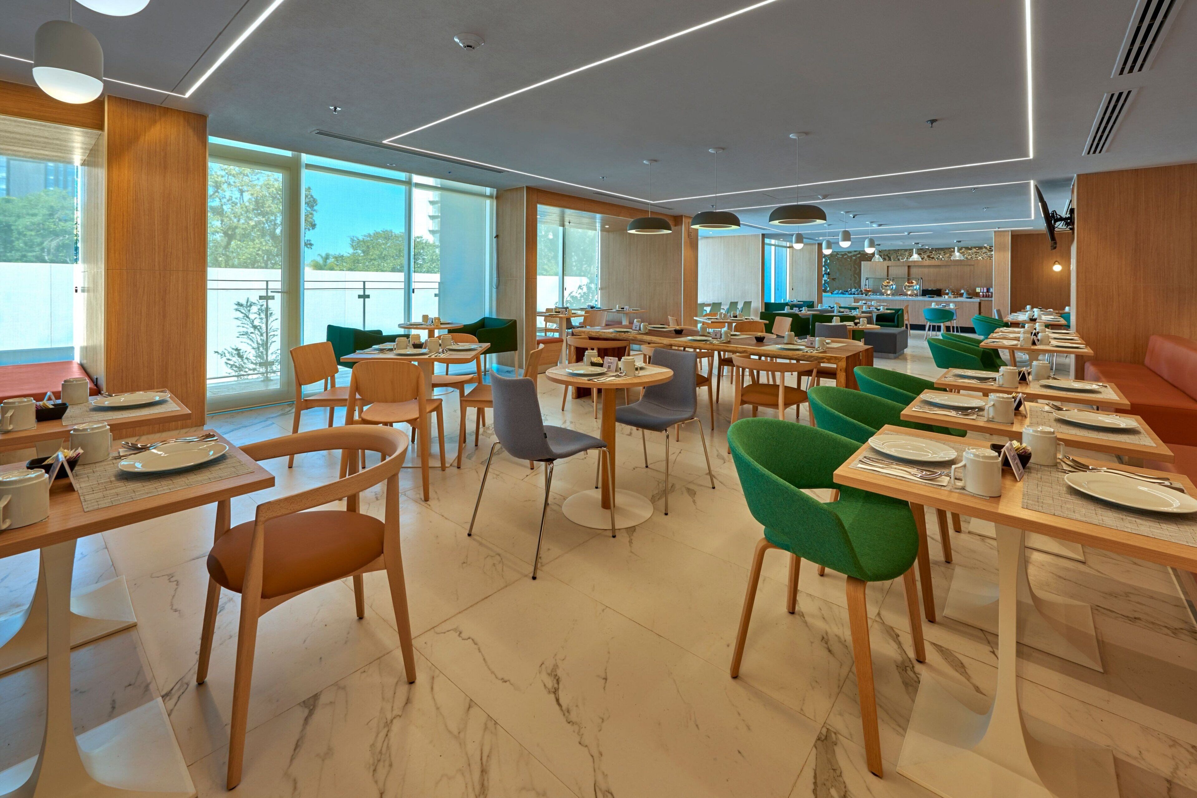 En moderne restaurant med flere spiseborde og stole, store vinduer og et rent, moderne interiør.