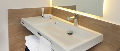 Un baño moderno con un lavamanos blanco, un espejo y un perchero para toallas.
