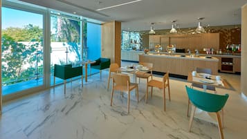 A modern kitchen with a marble floor, wooden cabinets, and a large island. There are two dining areas with green chairs and a table.