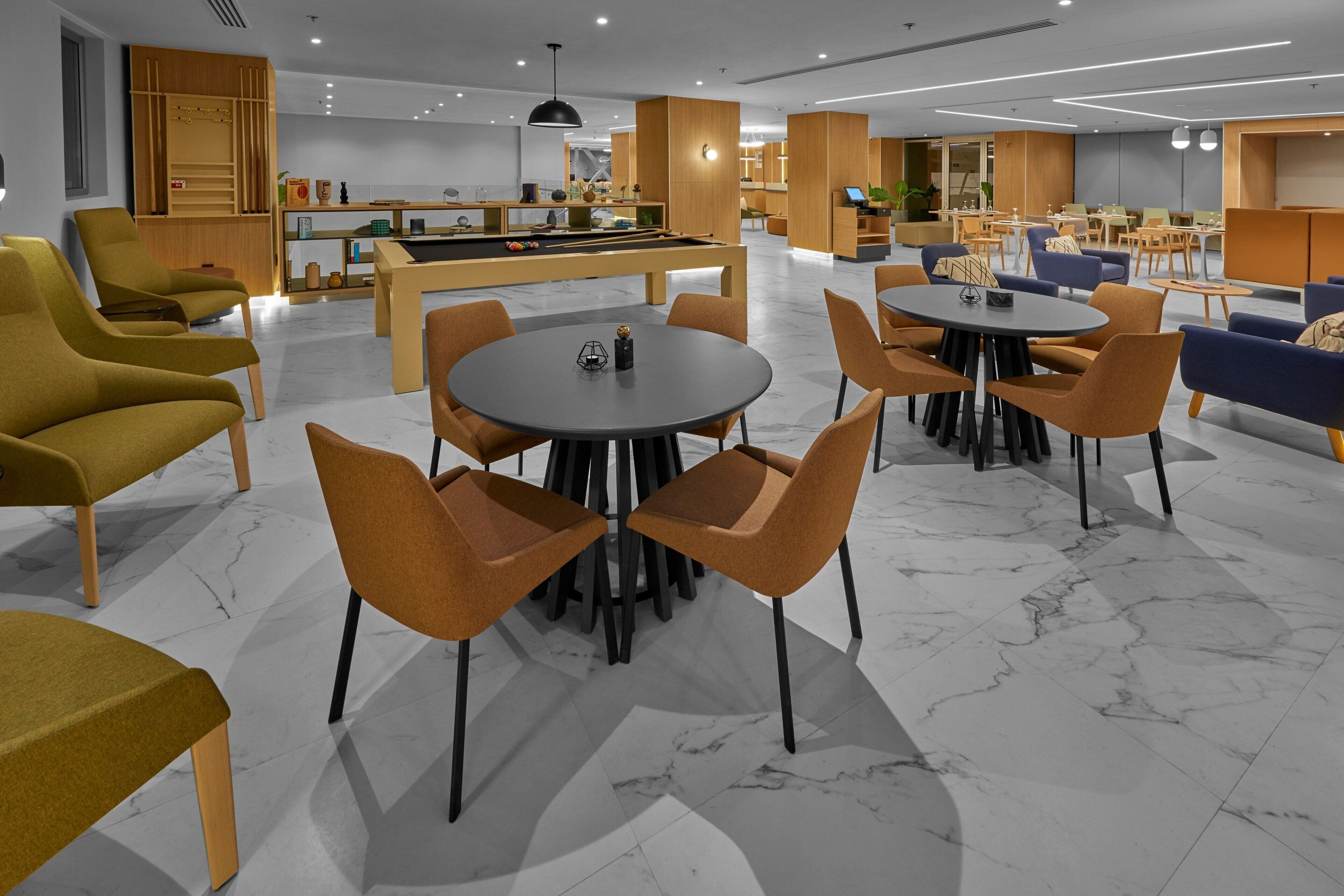 Ein moderner Loungebereich mit verschiedenen Sitzgelegenheiten, darunter Sofas und Sessel, der um einen zentral platzierten Billardtisch angeordnet ist.