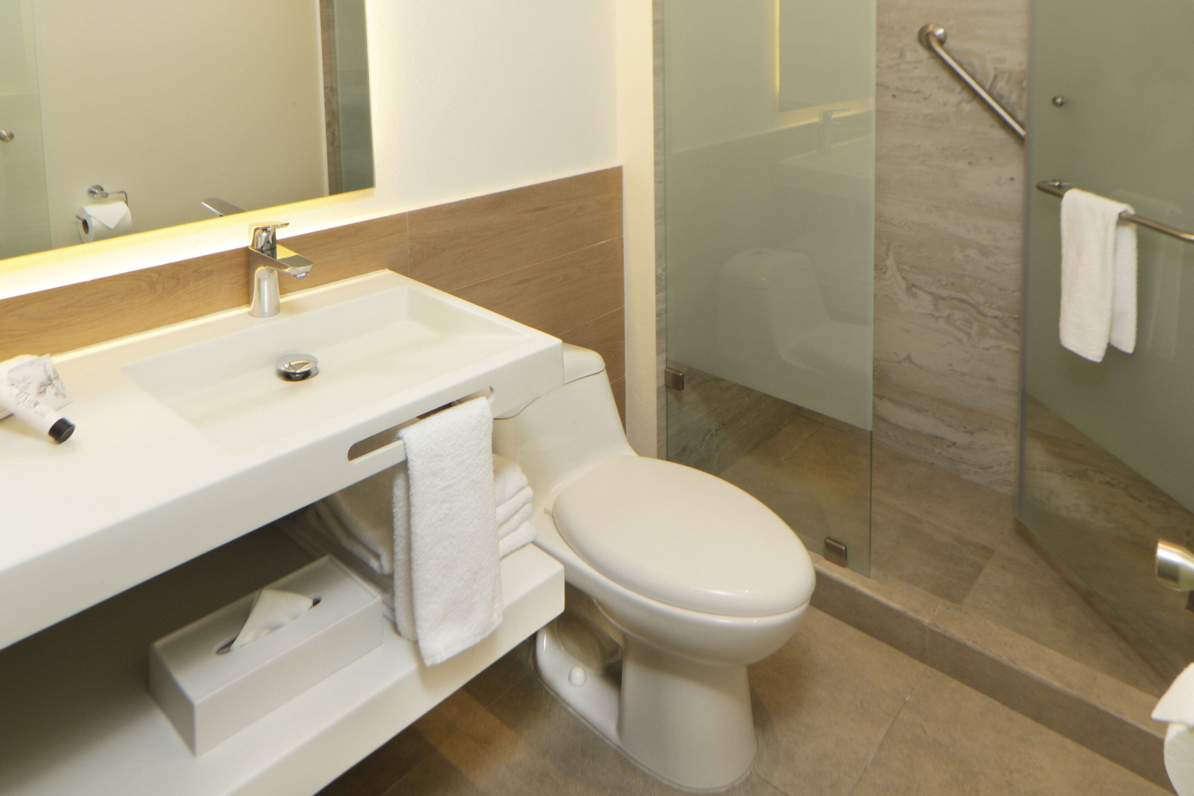 Un bany modern amb un rentapeus, un mirall i un vàter de color blanc. Inclou una cabina de dutxa de vidre amb barana.