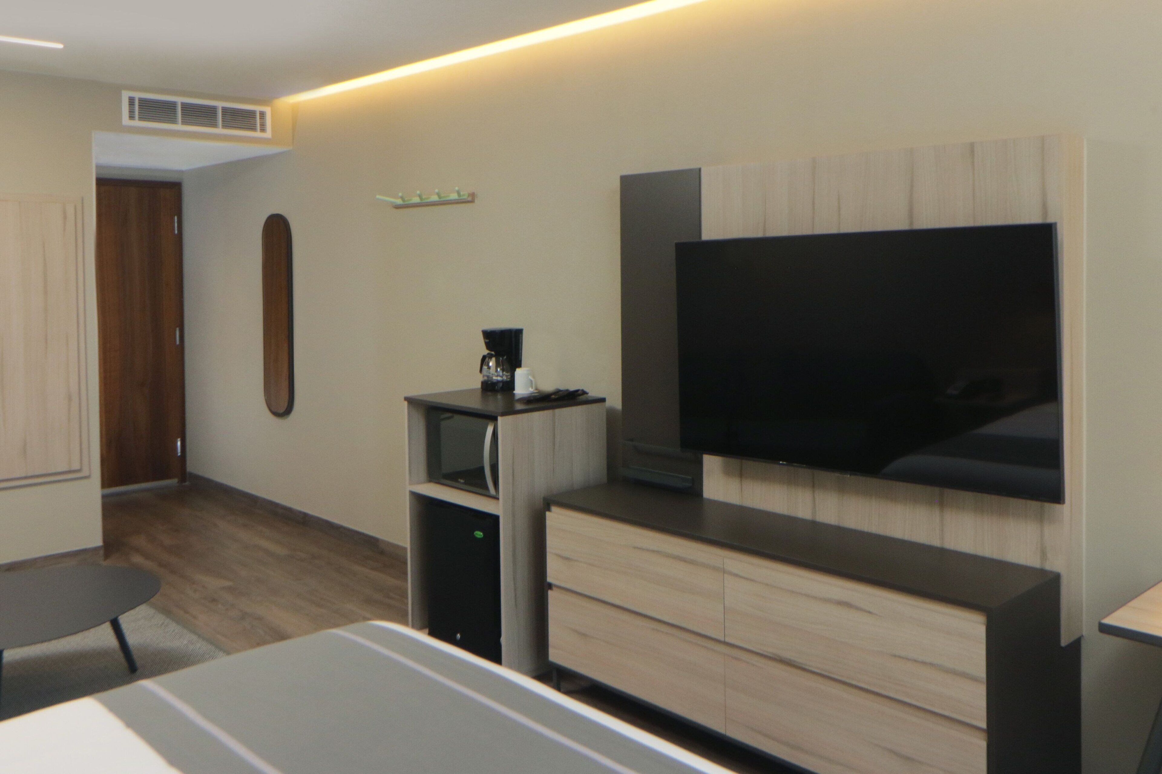 Une chambre d’hôtel moderne équipée d’un téléviseur à écran plat fixé au mur, d’une armoire en bois, d’une petite table et d’un bureau.