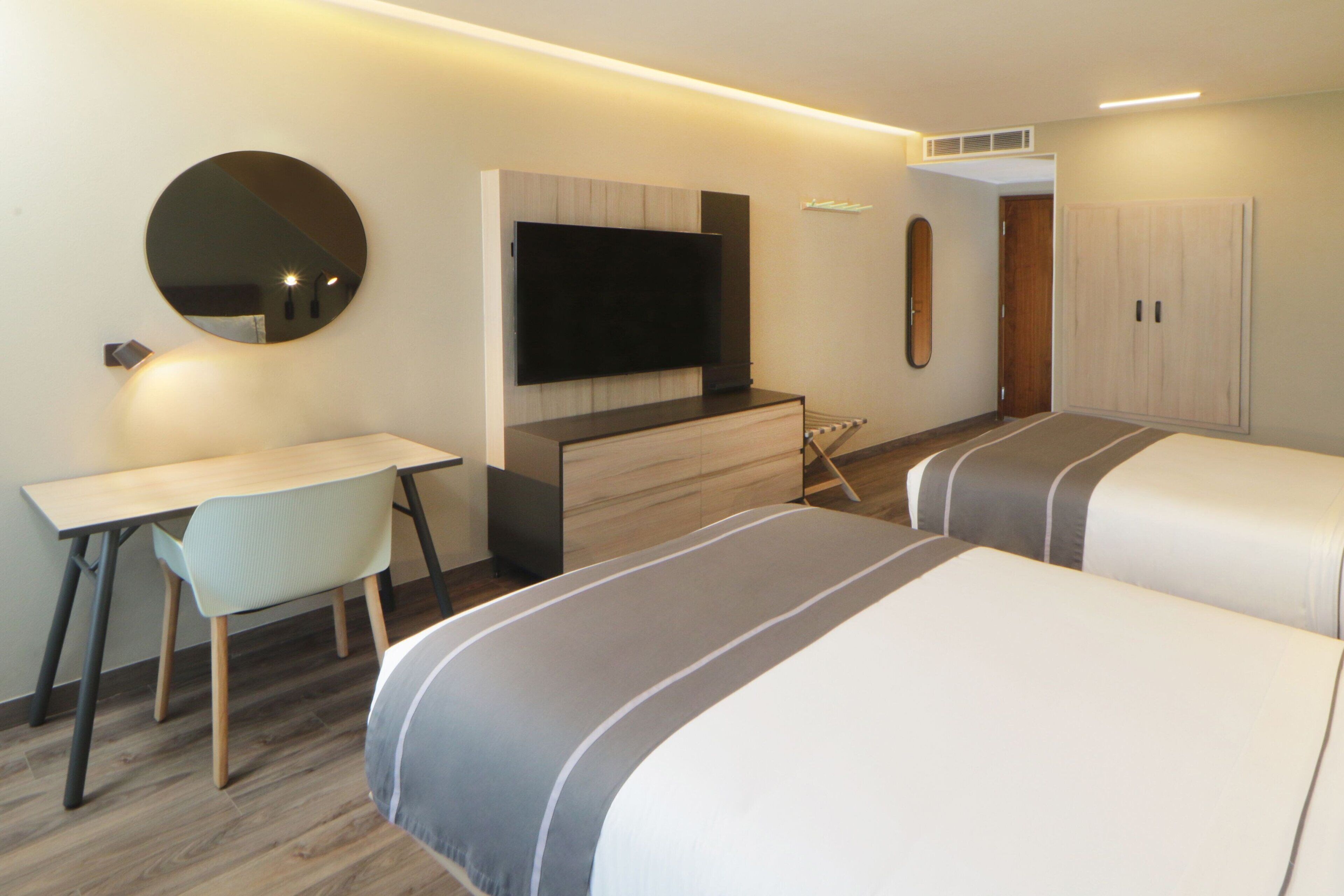 Una habitación de hotel moderna con una televisión de pantalla plana, un escritorio, una silla y dos camas con ropa de cama a rayas.