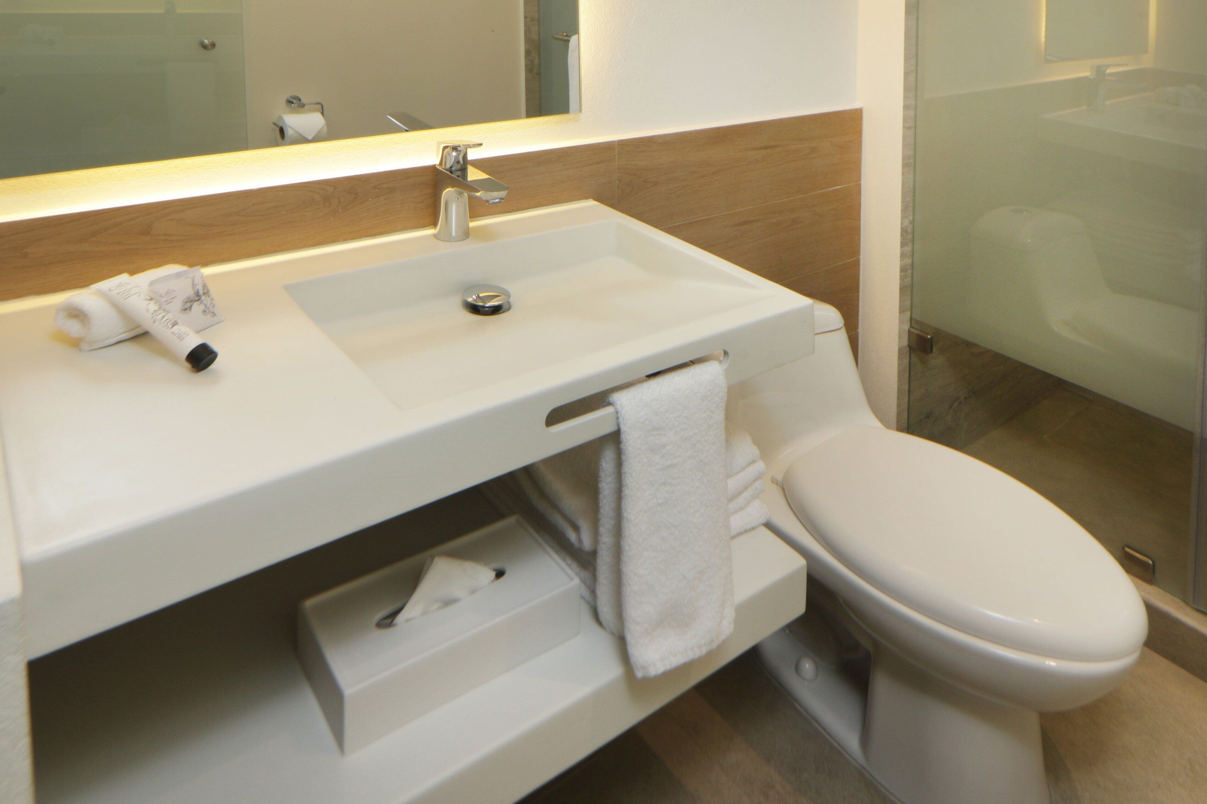 Un baño moderno con lavamanos, espejo y inodoro blancos.