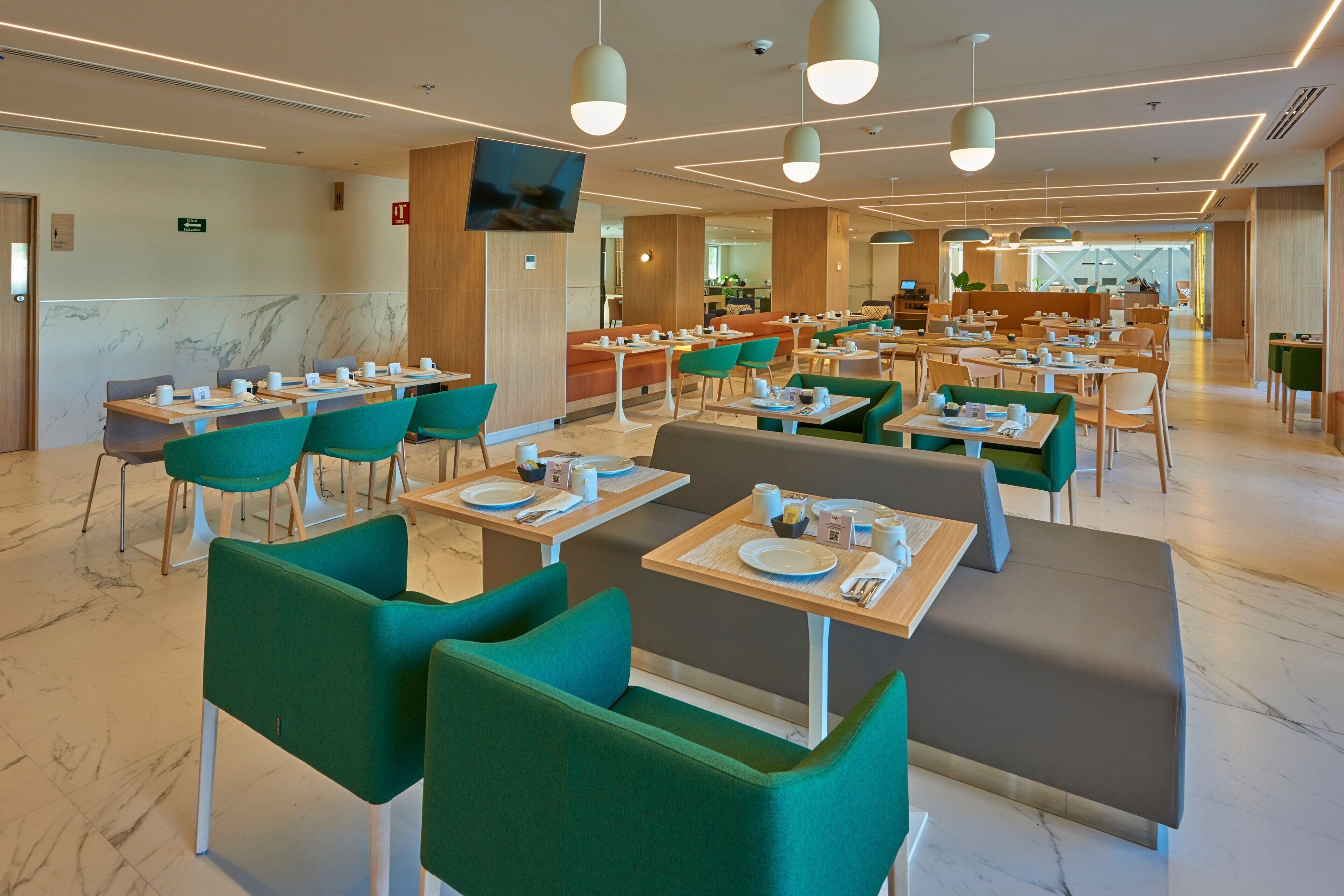 Un espace de restauration moderne avec des sièges verts et gris, un sol en marbre et un éclairage suspendu.