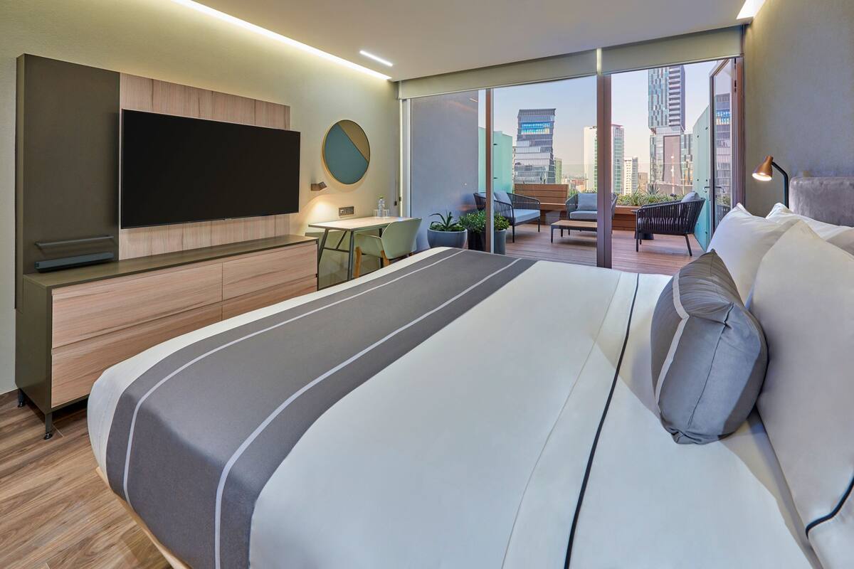 Camera d'albergo moderna con un letto grande, una TV a schermo piatto, una scrivania e un balcone vista città.