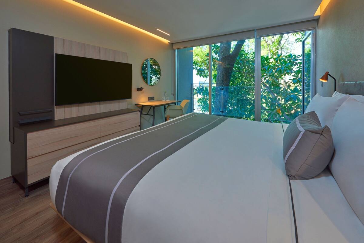 Una camera da letto moderna con un letto grande, una TV a parete, una scrivania e una finestra con vista sul verde.