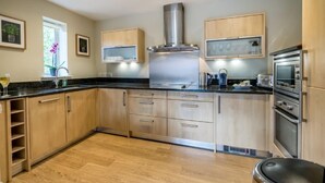 Une cuisine moderne avec des meubles en bois, des appareils électroménagers en acier inoxydable et une hotte aspirante centrale.