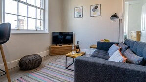 A modern living room with a large window, a flat-screen TV, a sofa, a coffee table, and a small side table. - Riverside City Loft Apartment (York)