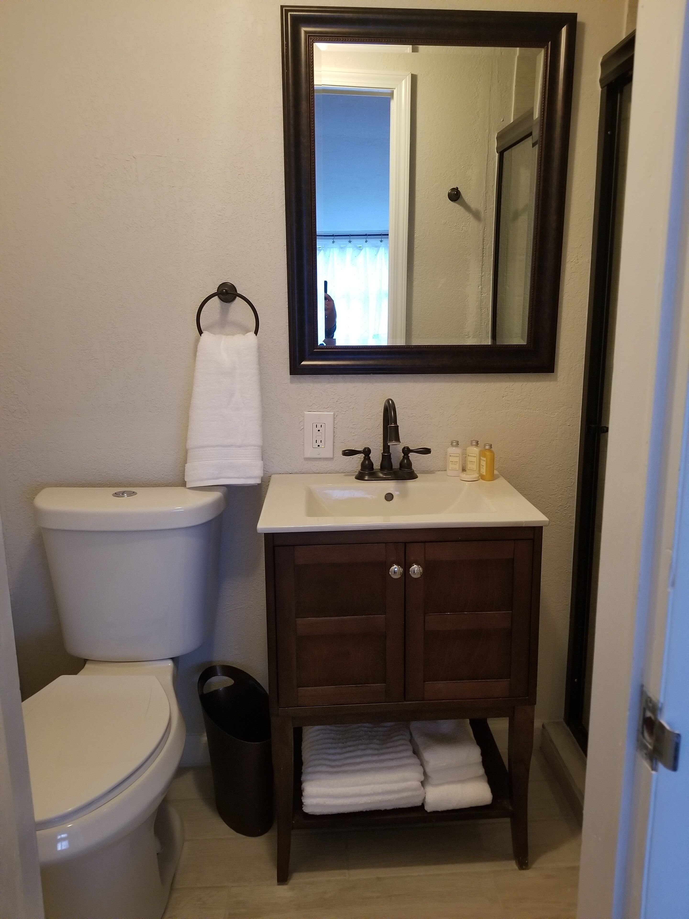 Un baño con inodoro, lavamanos, espejo y toallero.