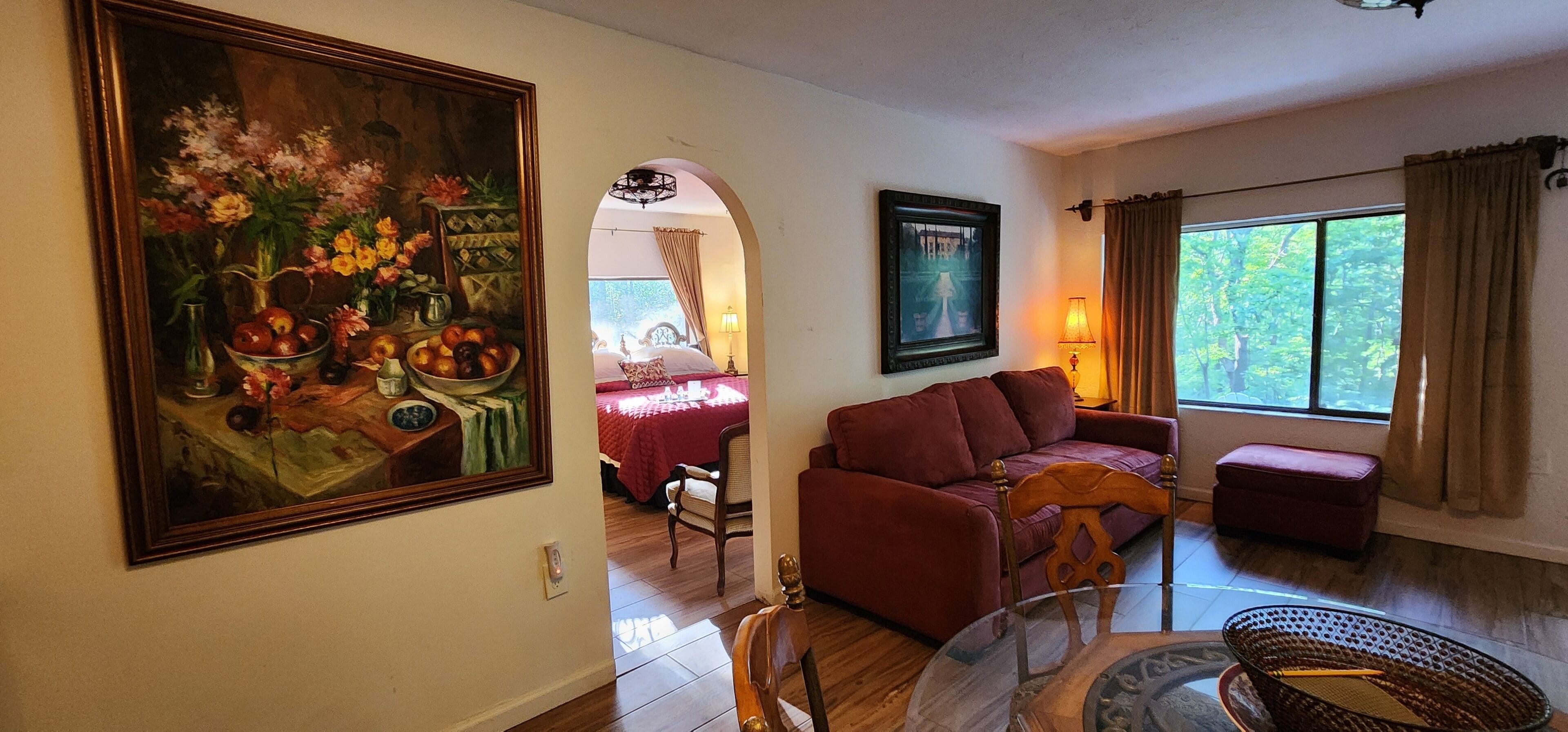 A living room with a sofa, a dining table with chairs, a painting, and a window with curtains.