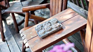 Una panca di legno con un sottobicchiere di pietra e una pianta in vaso con fiori rosa.