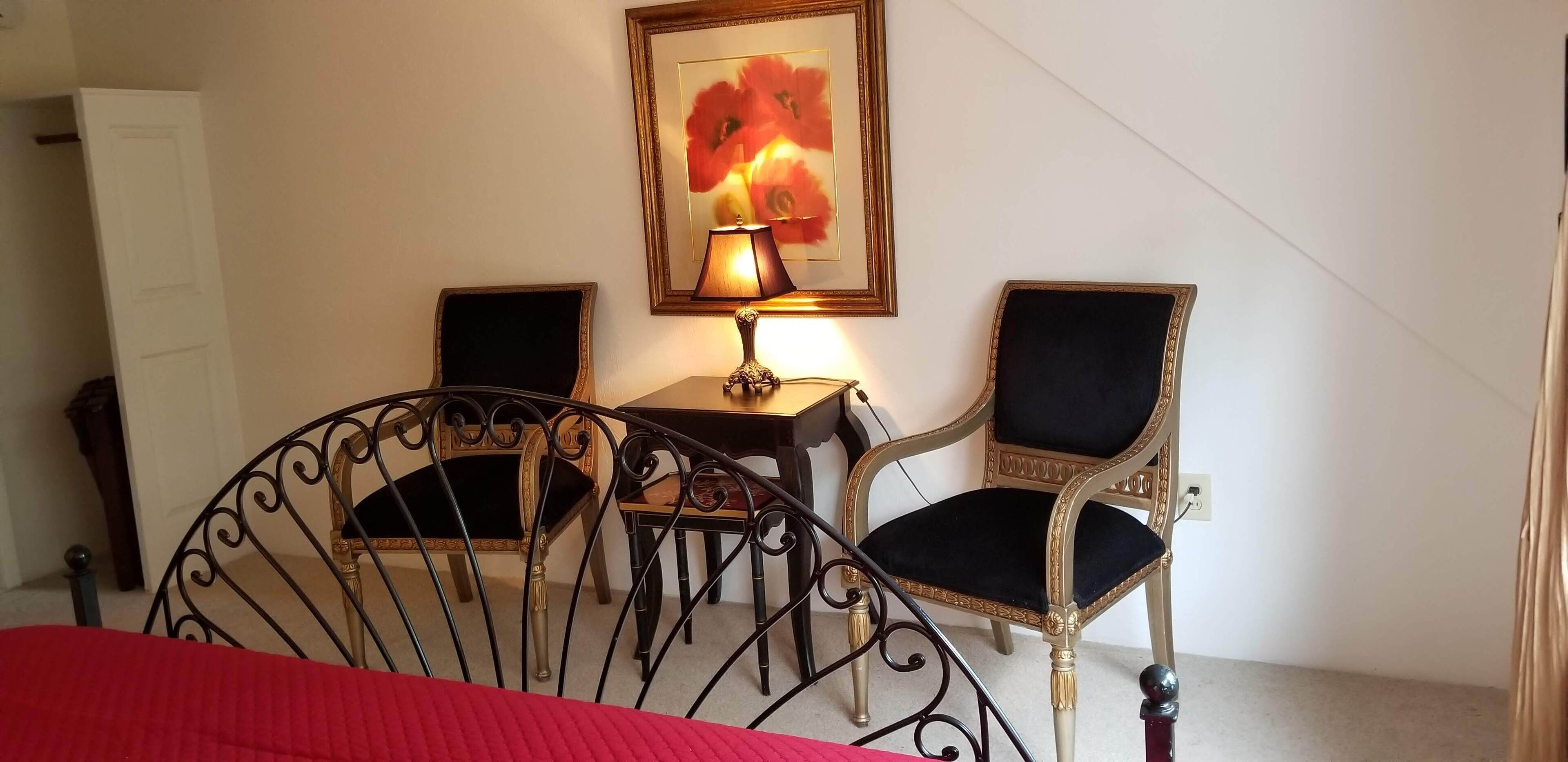 A bedroom with a bed, two chairs, a small table, a lamp, and a framed picture on the wall.