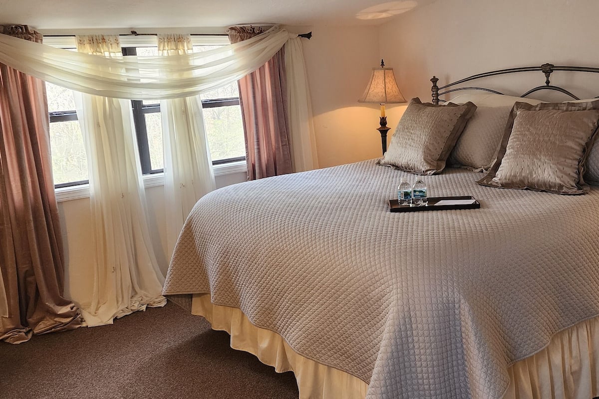 A neatly made bed with a quilted cover, two bedside lamps, and a tray with a glass and a book.