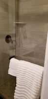 Una ducha con mampara de cristal, azulejos color beige y una toalla blanca colgada en un perchero.