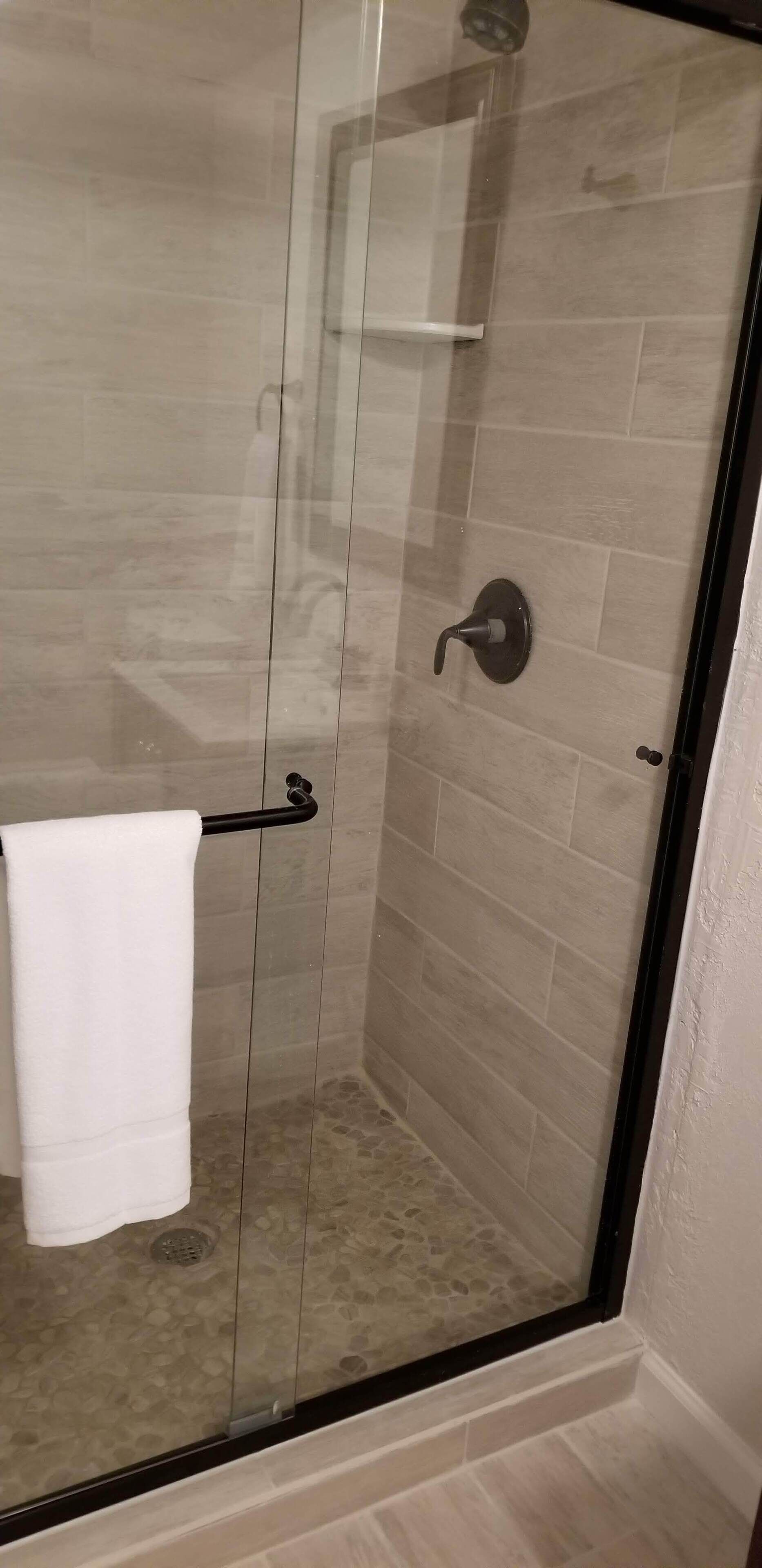 A glass-enclosed shower with beige tiles and a white towel on a rack.