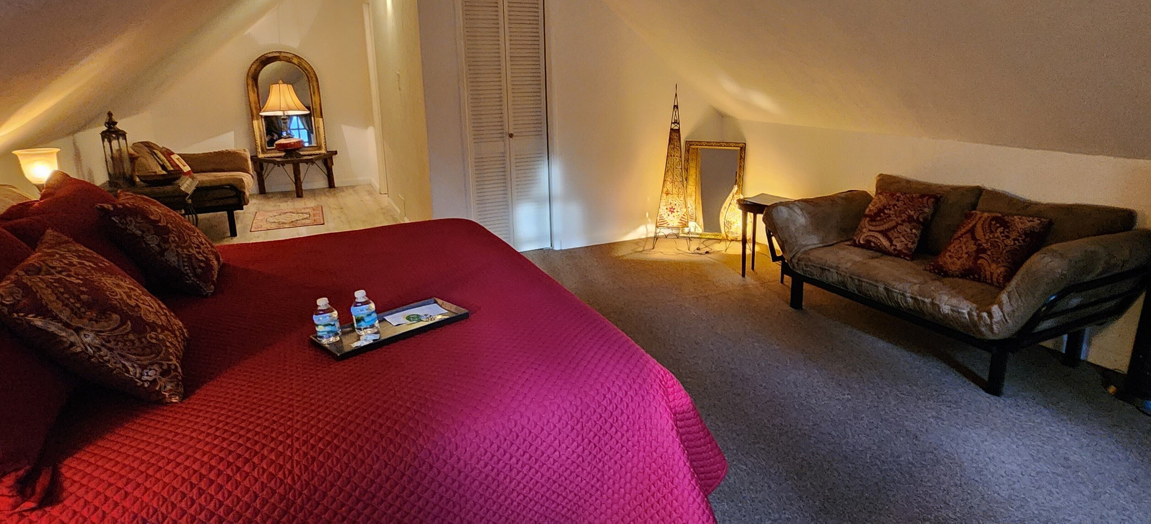 A bedroom with a large bed, a leather sofa, a mirror, and a lamp.
